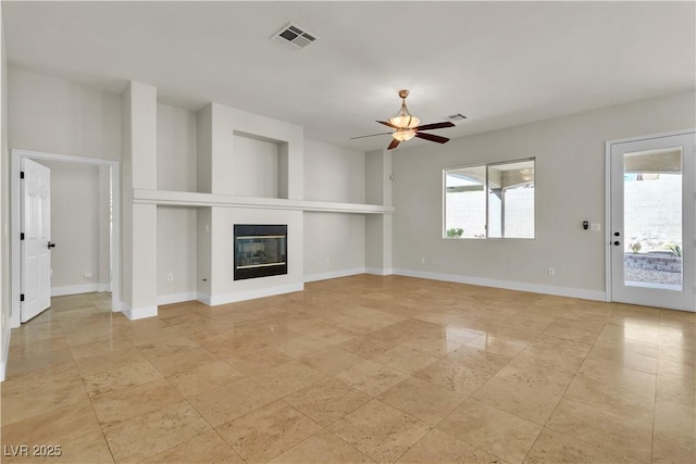 11621 La Mirago Pl, Las Vegas, NV 89138 - unfurnished living room featuring a ceiling fan, healthy amount of natural light, a glass covered fireplace, and baseboards