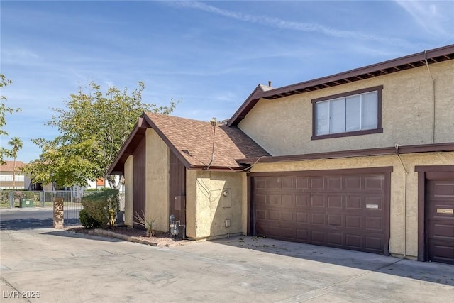 view of side of property featuring a garage, driveway, stucco siding, a shingled roof, and fence