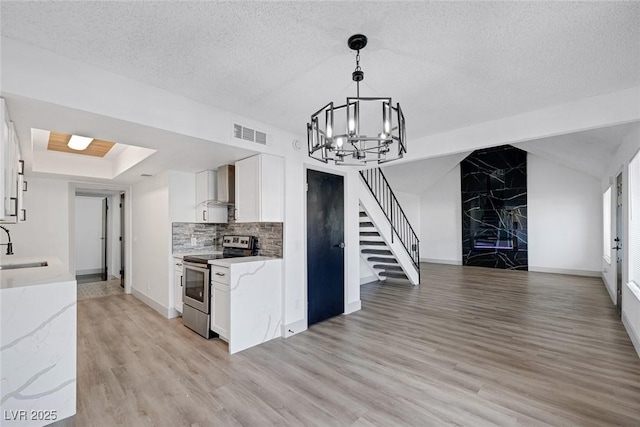 kitchen with stainless steel electric stove, wall chimney range hood, a chandelier, light wood-style floors, and a textured ceiling