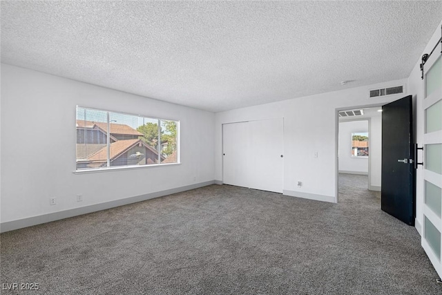 unfurnished bedroom featuring multiple windows, carpet, a barn door, a textured ceiling, and a closet