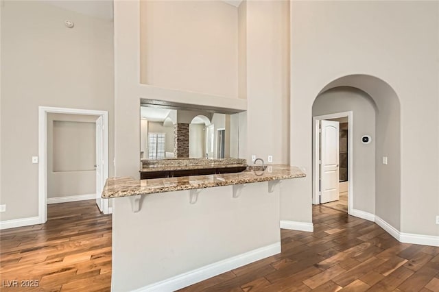 8124 Bay Harbor Dr, Las Vegas, NV 89128 - kitchen with a towering ceiling, a kitchen bar, a peninsula, dark wood-type flooring, and light stone counters