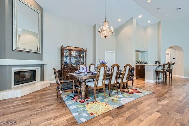 8124 Bay Harbor Dr, Las Vegas, NV 89128 - dining space with high vaulted ceiling, arched walkways, a chandelier, light wood-style flooring, and a tile fireplace