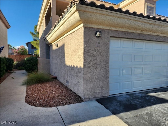 view of side of home featuring stucco siding, a tile roof, an attached garage, and driveway