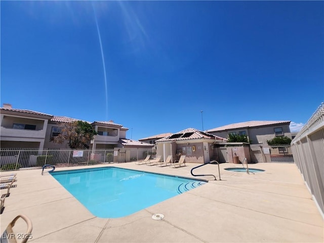 community pool with a patio area, fence, and a hot tub