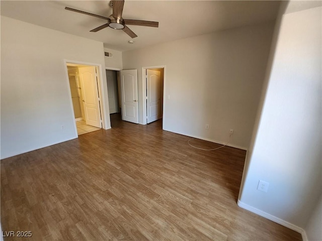 unfurnished bedroom with wood finished floors, baseboards, a walk in closet, ceiling fan, and connected bathroom