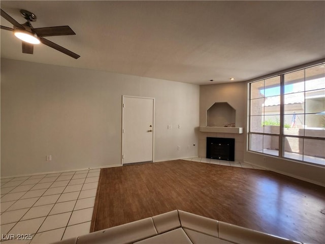 unfurnished living room featuring light wood finished floors, ceiling fan, a fireplace, and baseboards