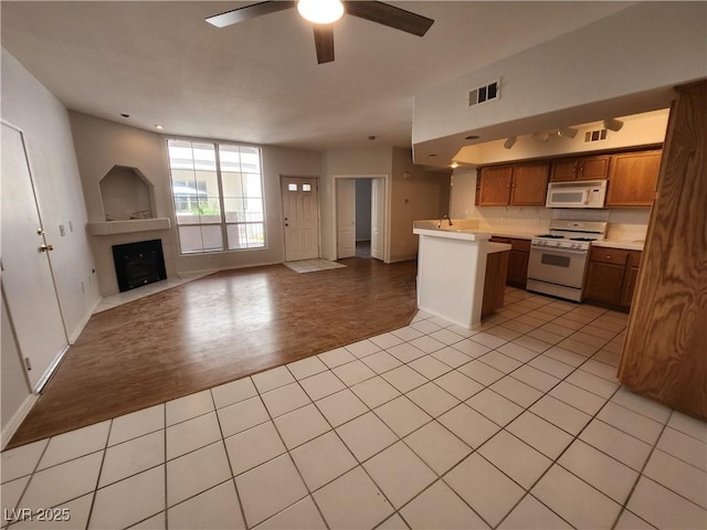 kitchen with white appliances, open floor plan, ceiling fan, light countertops, and a fireplace with flush hearth