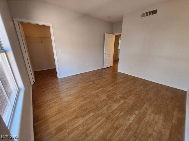 unfurnished bedroom with a walk in closet, wood finished floors, and a closet