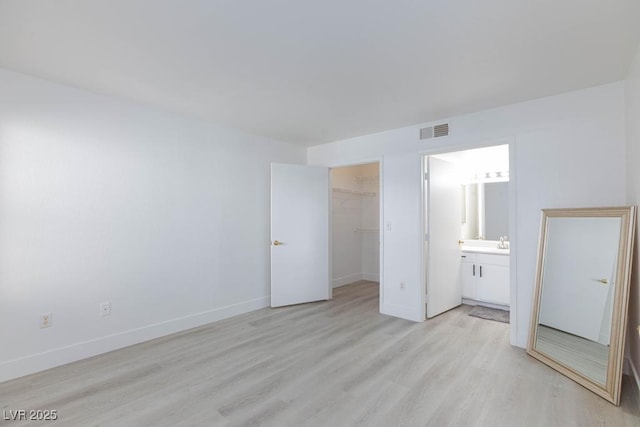 unfurnished bedroom featuring light wood finished floors, baseboards, a walk in closet, and a closet