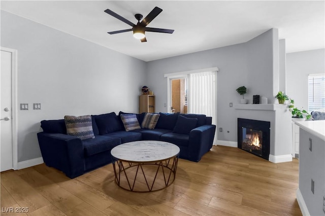 living area featuring light wood-style floors, a ceiling fan, a glass covered fireplace, and baseboards