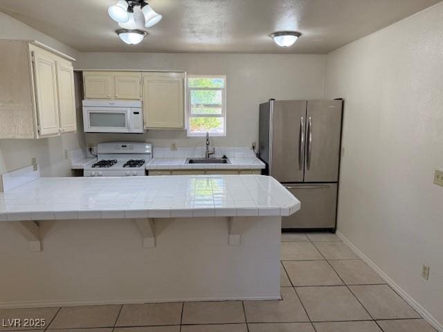 kitchen with white appliances, tile countertops, a sink, a peninsula, and a kitchen bar