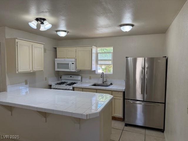 kitchen featuring white appliances, a sink, a peninsula, tile counters, and light tile patterned floors