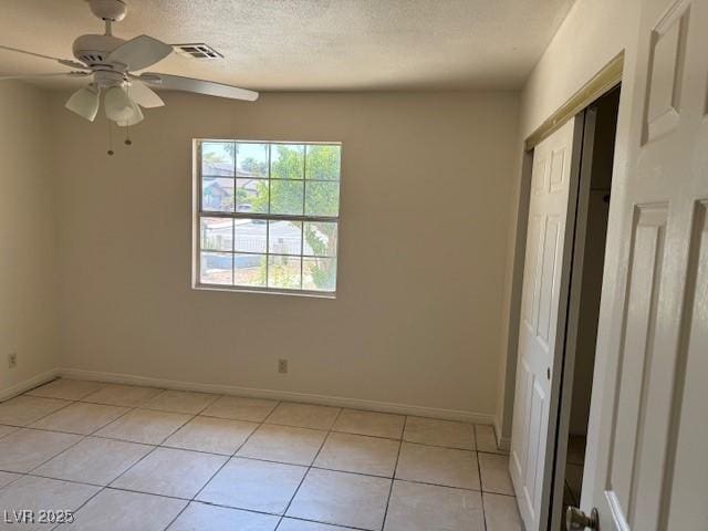unfurnished bedroom with light tile patterned floors, baseboards, a closet, ceiling fan, and a textured ceiling