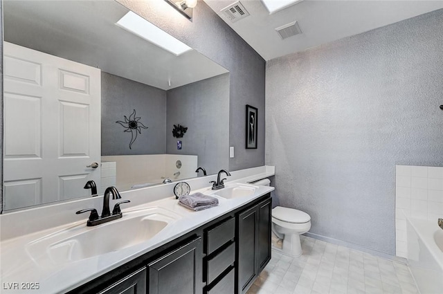 bathroom featuring a textured wall, a bath, toilet, double vanity, and baseboards