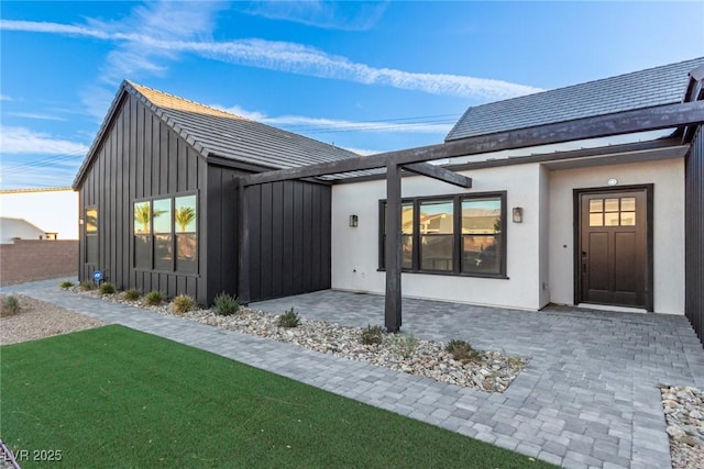 back of house with a patio area, board and batten siding, stucco siding, and fence