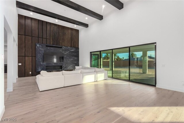 unfurnished living room featuring beam ceiling, light wood finished floors, a towering ceiling, baseboards, and a fireplace