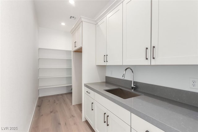 kitchen featuring a sink, recessed lighting, light wood-type flooring, white cabinetry, and dark countertops