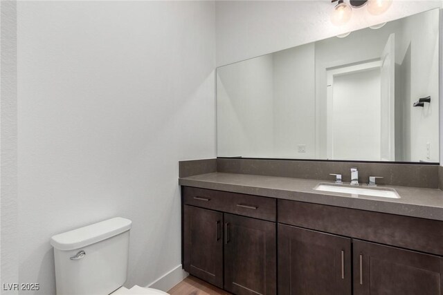 half bathroom with toilet, vanity, baseboards, and wood finished floors