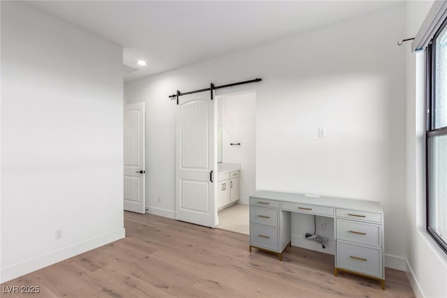 unfurnished office with light wood-type flooring, recessed lighting, a barn door, and baseboards