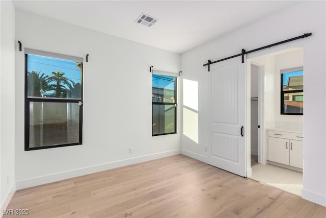 unfurnished room with a barn door, light wood-style floors, and baseboards