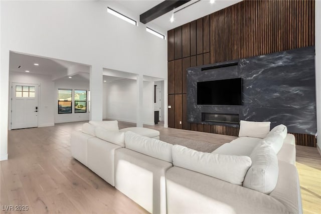 living room with light wood finished floors, beam ceiling, a towering ceiling, a high end fireplace, and baseboards