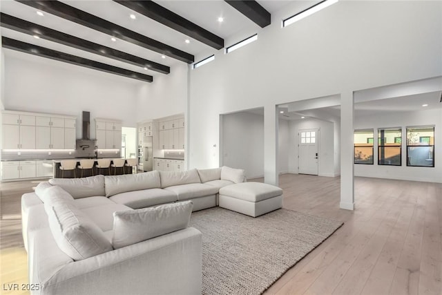 living area featuring a towering ceiling, beam ceiling, and light wood-type flooring