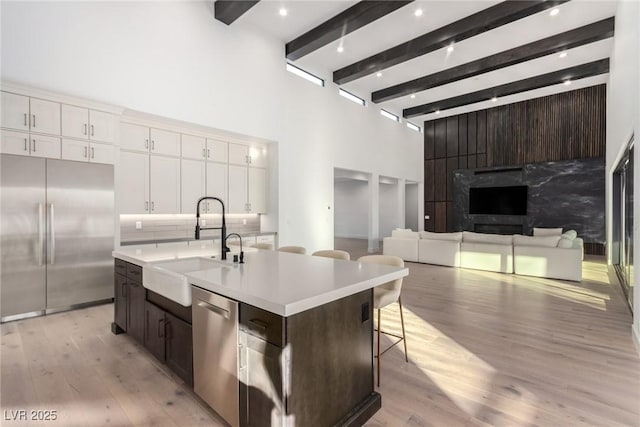 kitchen featuring stainless steel appliances, a sink, light countertops, white cabinetry, and beamed ceiling