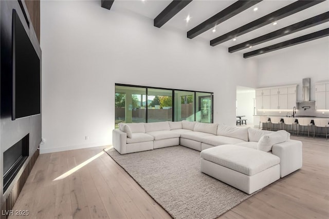 living area with a towering ceiling, beam ceiling, light wood-type flooring, baseboards, and recessed lighting