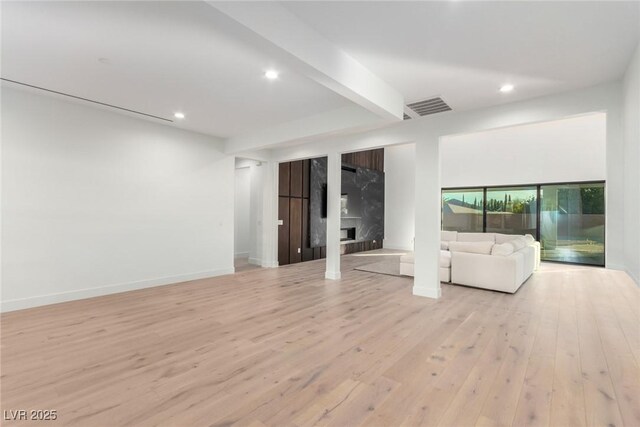 unfurnished living room featuring a high end fireplace, light wood finished floors, recessed lighting, baseboards, and beamed ceiling