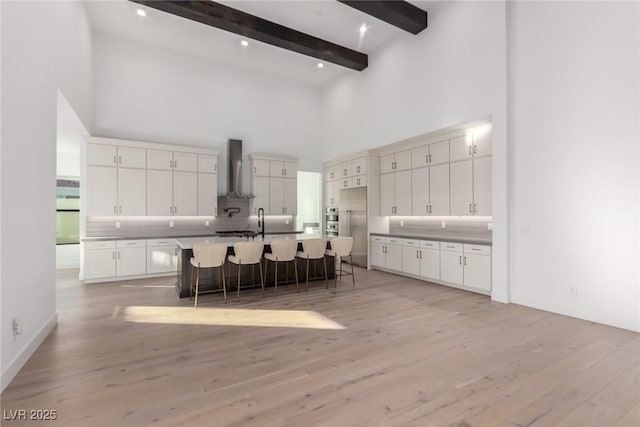 kitchen with a high ceiling, tasteful backsplash, a breakfast bar, light wood-style flooring, and beam ceiling