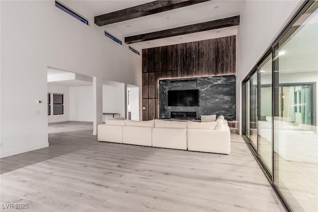 unfurnished living room featuring a high ceiling, light wood-type flooring, a premium fireplace, and beam ceiling