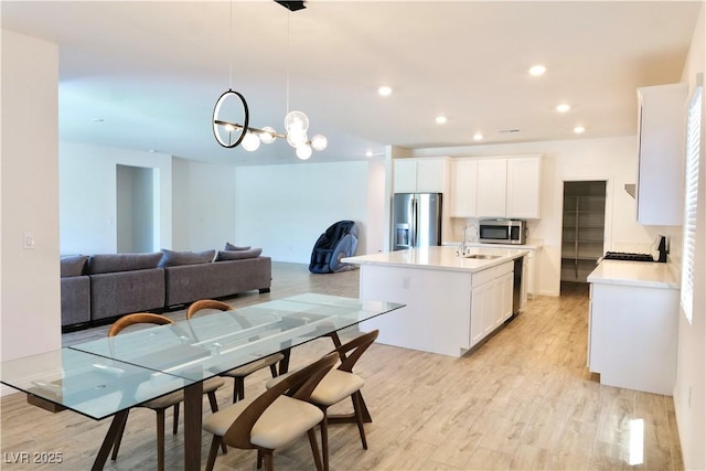 6250 Lamont Hills Ave, Las Vegas, NV 89139 - kitchen with appliances with stainless steel finishes, white cabinets, a chandelier, light wood finished floors, and a kitchen island with sink