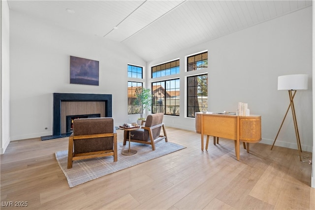 living area featuring light wood finished floors, a warm lit fireplace, baseboards, and high vaulted ceiling
