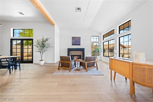 dining space with light wood-style flooring, plenty of natural light, a lit fireplace, and french doors