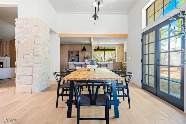 dining room with a towering ceiling, light wood-type flooring, and a lit fireplace