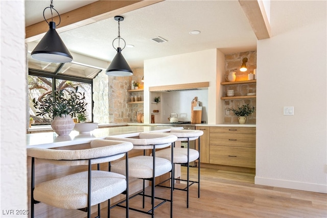kitchen with open shelves, decorative light fixtures, light wood-type flooring, and light countertops