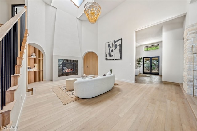 living room with a high ceiling, a glass covered fireplace, wood finished floors, and baseboards