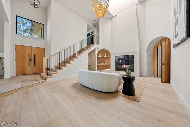 entrance foyer with a high ceiling, stairway, wood finished floors, a glass covered fireplace, and baseboards