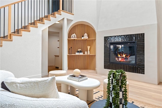 interior space featuring a high ceiling, built in features, a glass covered fireplace, wood finished floors, and stairway