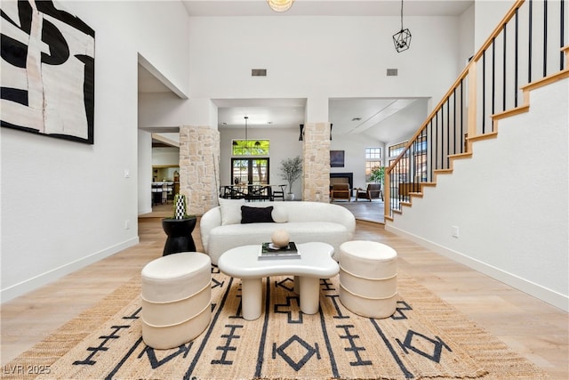 living area with wood finished floors, ornate columns, baseboards, a glass covered fireplace, and a high ceiling