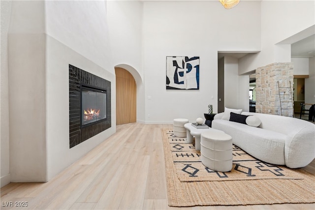 living room featuring a high ceiling, wood finished floors, a glass covered fireplace, baseboards, and ornate columns