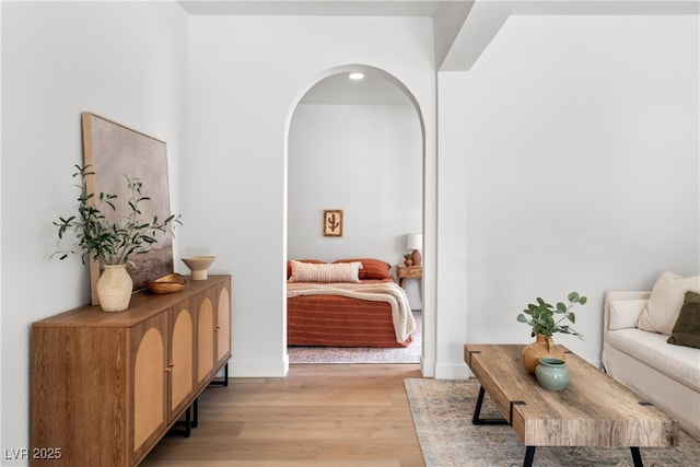 living area featuring light wood-style flooring, arched walkways, and baseboards