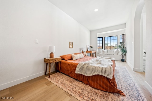 bedroom featuring light wood finished floors, arched walkways, and baseboards