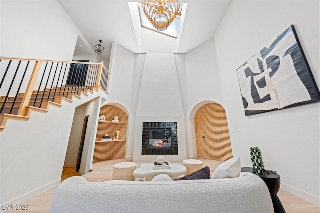 living room with a towering ceiling, wood finished floors, baseboards, a tiled fireplace, and stairs