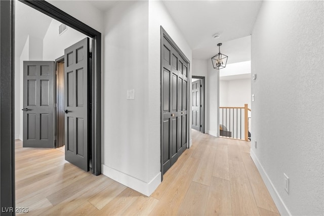 corridor with light wood finished floors, baseboards, a chandelier, and a textured wall