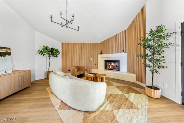living area featuring a glass covered fireplace, light wood-type flooring, a chandelier, baseboards, and wood walls