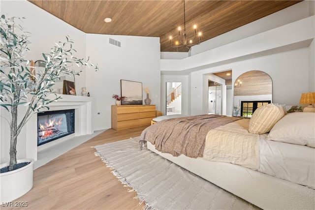 bedroom featuring a glass covered fireplace, wooden ceiling, wood finished floors, a chandelier, and recessed lighting