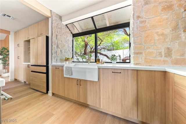 kitchen featuring light brown cabinetry, light wood-type flooring, light countertops, a sink, and modern cabinets
