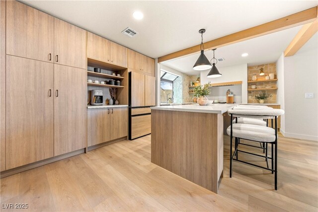 kitchen featuring open shelves, fridge, light brown cabinetry, a breakfast bar, and light wood-type flooring