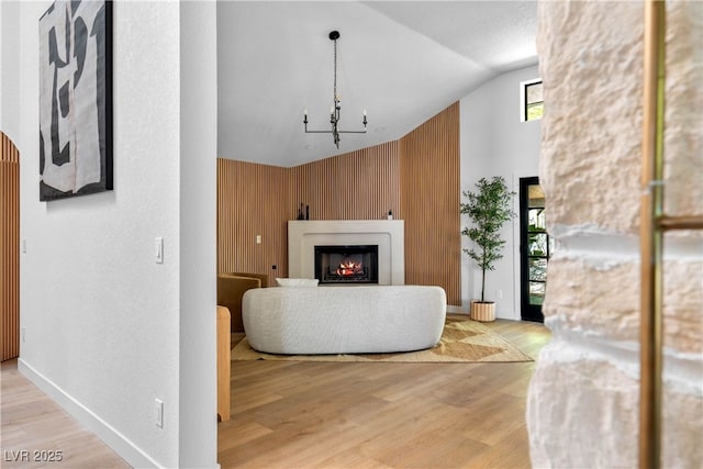 living area featuring a warm lit fireplace, high vaulted ceiling, wood finished floors, a chandelier, and wood walls
